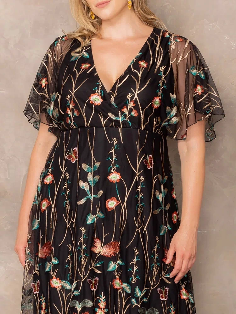 Sonnet Embroidered Midi Cocktail Dress in Onyx Meadow Print  Close-up of plus size model wearing black embroidered mesh dress with V-neckline and sheer flutter sleeves, showing floral and butterfly embroidery details.