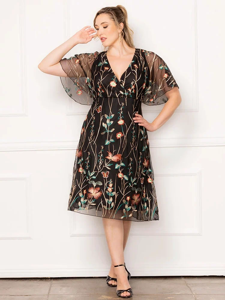 Sonnet Embroidered Midi Cocktail Dress in Onyx Meadow Print  Plus size model wearing black embroidered mesh dress with V-neckline and sheer flutter sleeves, styled for a wedding guest or special occasion.