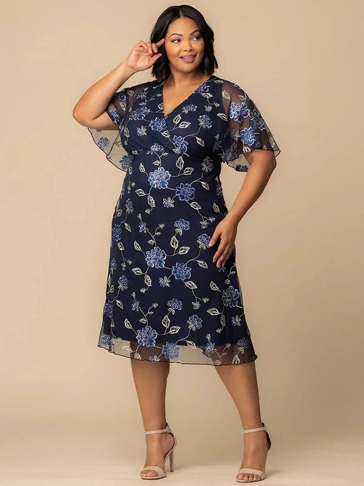 Sonnet Embroidered Midi Cocktail Dress in Navy Blue Blooms  Plus size model wearing navy blue embroidered mesh dress with V-neckline and sheer flutter sleeves, styled for a wedding guest or formal event.