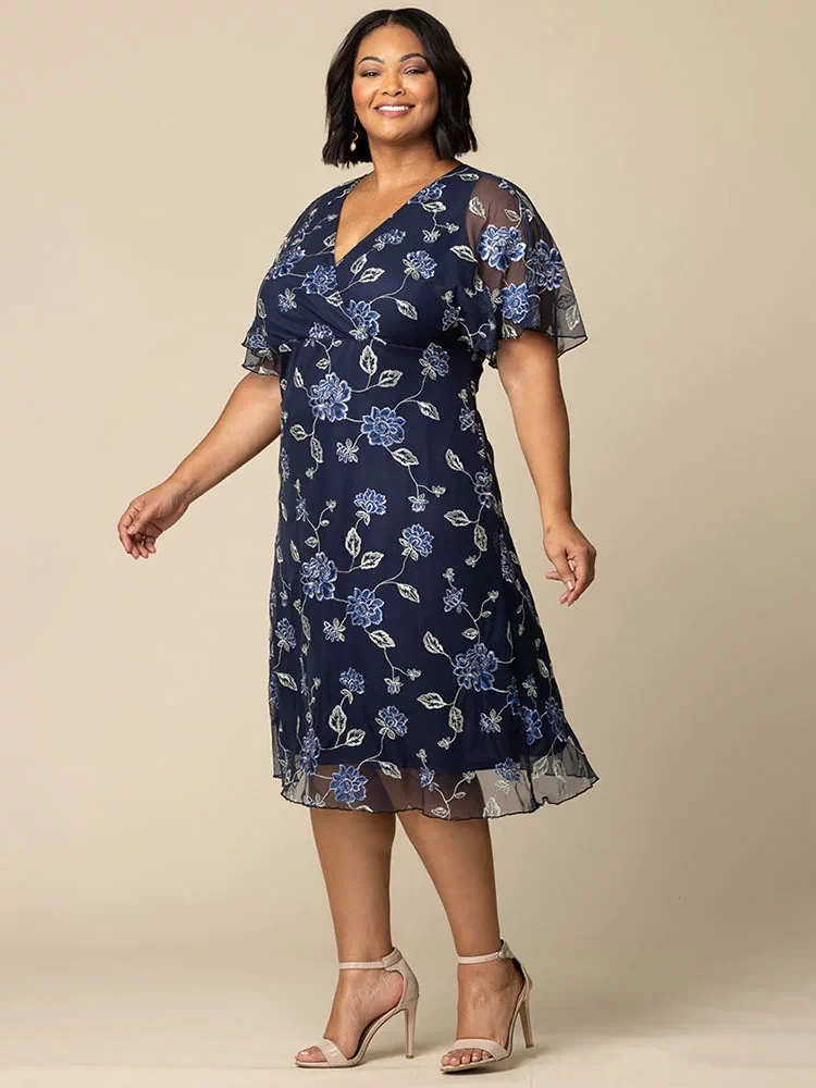 Sonnet Embroidered Midi Cocktail Dress in Navy Blue Blooms  Plus size model in navy blue embroidered mesh midi dress with V-neck and sheer flutter sleeves, flattering fit for weddings, cocktail parties, and special events.