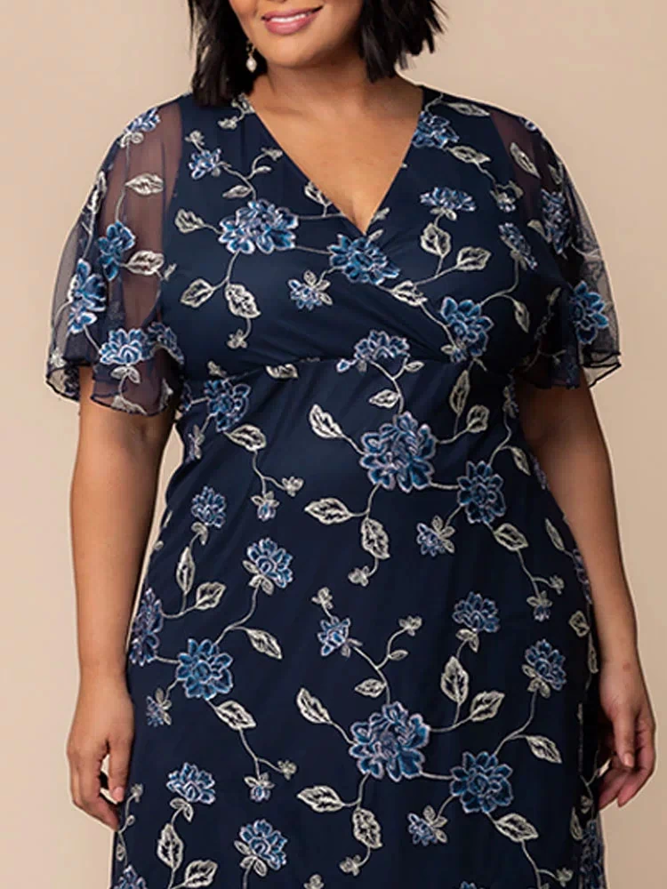 Sonnet Embroidered Midi Cocktail Dress in Navy Blue Blooms  Close-up of plus size model wearing navy blue embroidered mesh wrap dress with V-neckline and sheer flutter sleeves, showing floral detailing for special occasion wear.