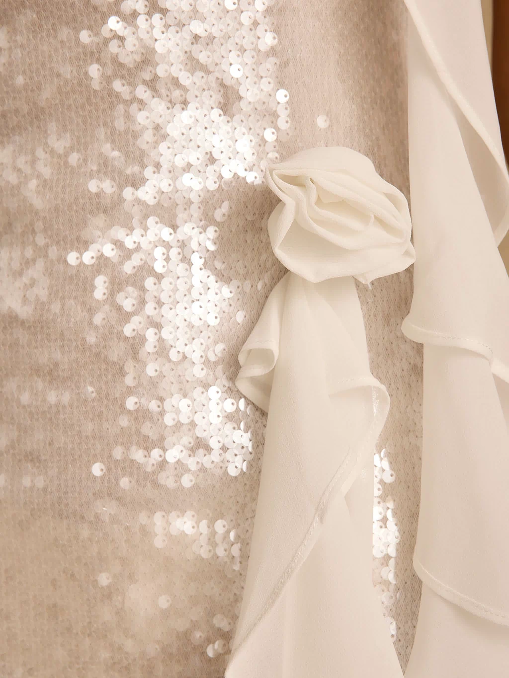 Close-up of rosette and chiffon frill trim on the white sequin mini dress.
