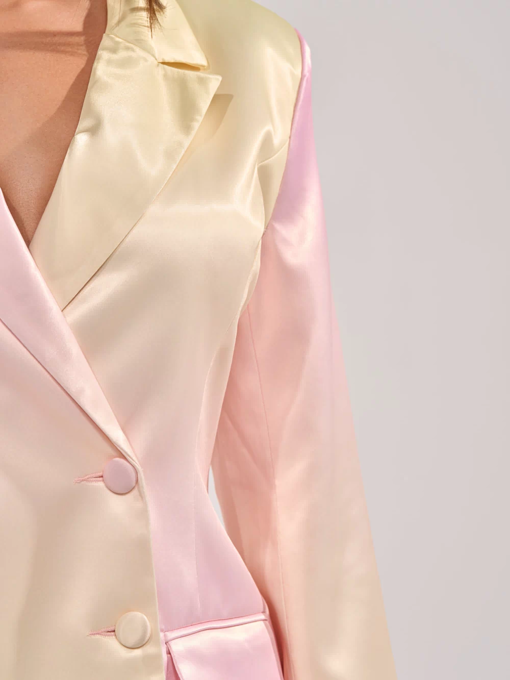 Close-up of a person wearing the SWEET TALK SATIN BLAZER, featuring a pastel cream and light pink gradient, notched collar, two buttons, and a flap front pocket for an elegant touch.