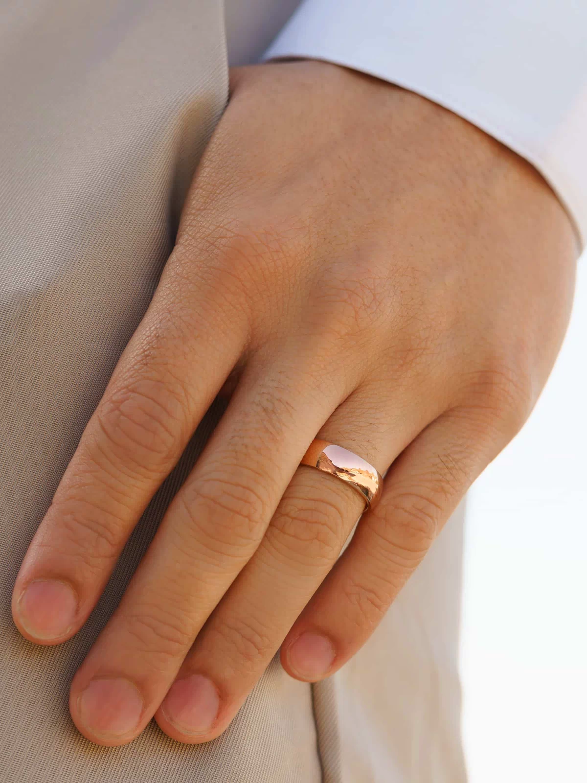 stunning rose gold affordable unisex horizon wedding band on men's hand with white shirt and tan pants