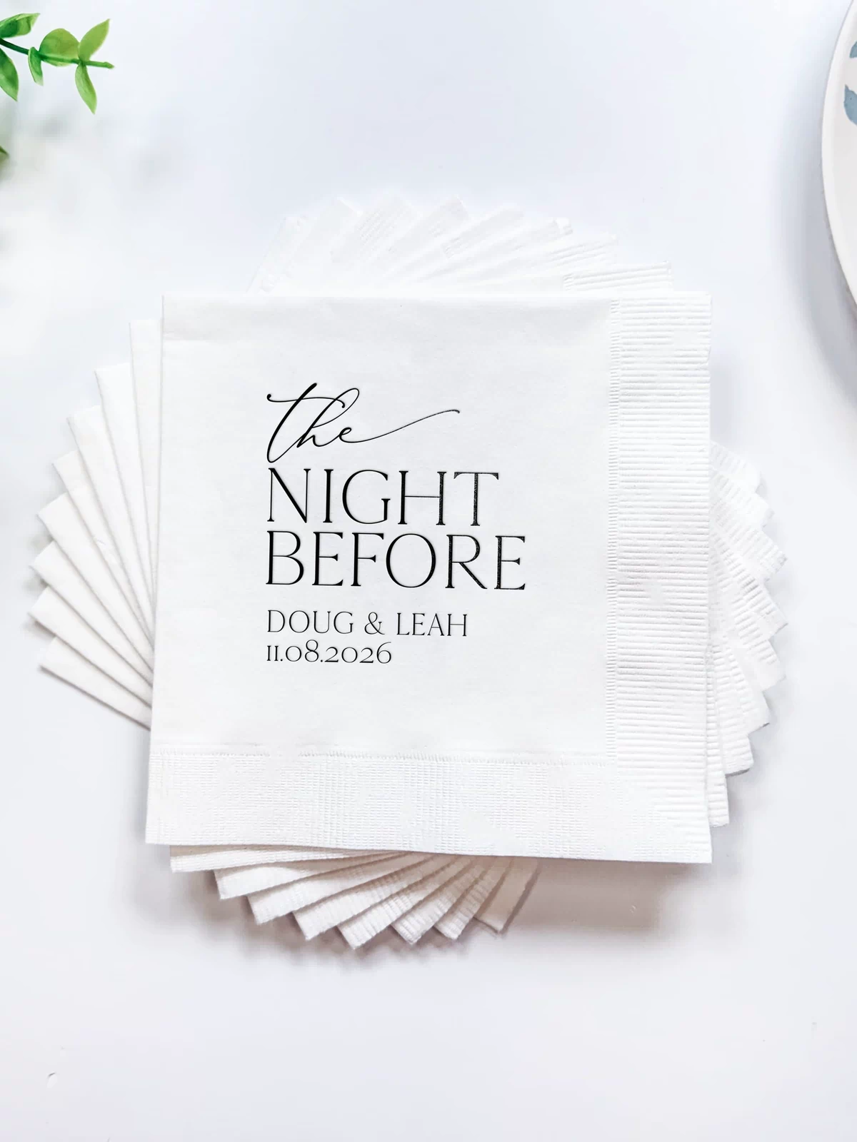 White napkins with "The Night Before" text and personalized names Doug & Leah with wedding date 11.08.2026 in black foil stamping