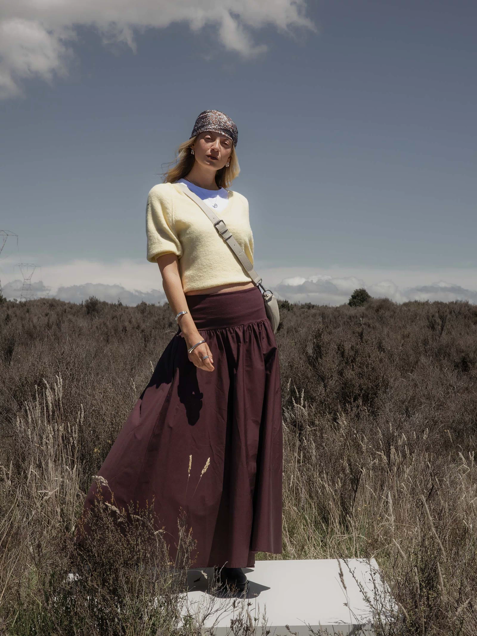 Person in yellow sweater and The Ultimate Skirt by Max standing outdoors in a grassy field.