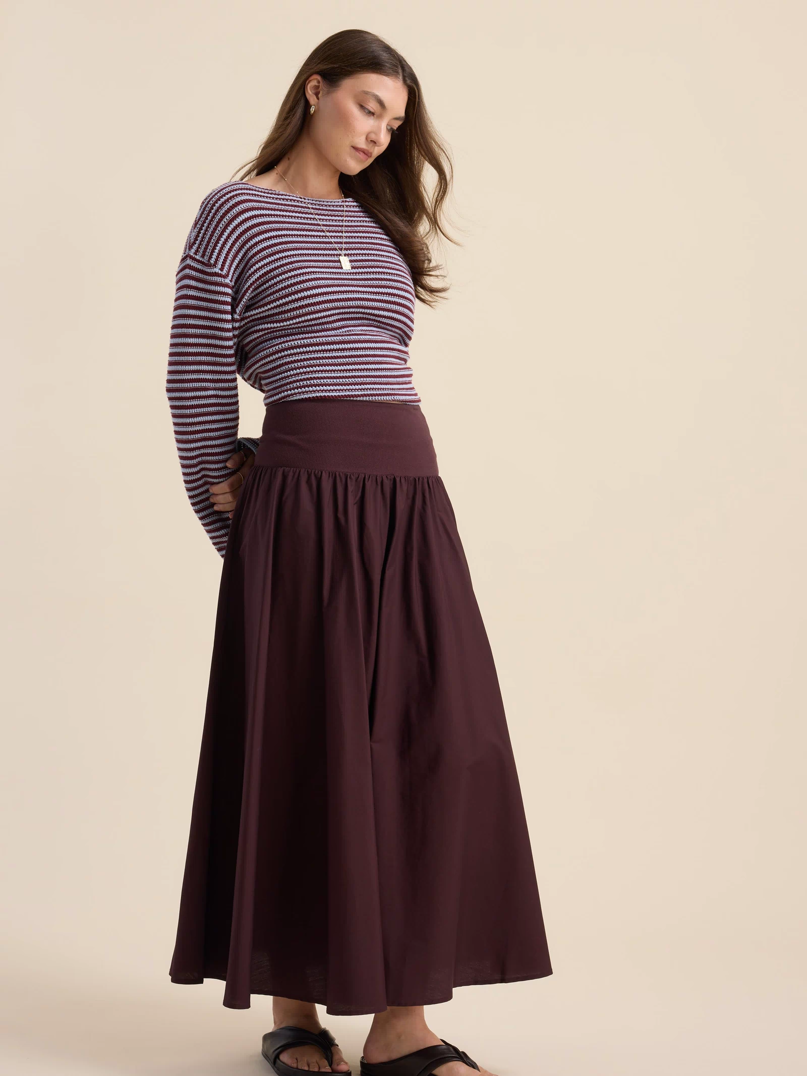Woman in striped sweater and Max’s The Ultimate Skirt, standing and looking down.