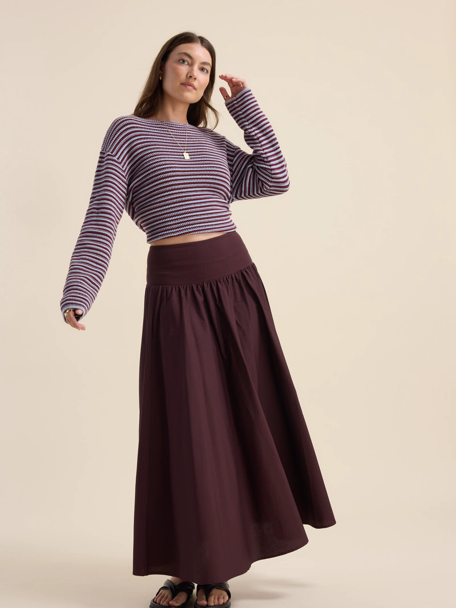 Woman in Max’s The Ultimate Skirt and striped crop top stands on beige background.
