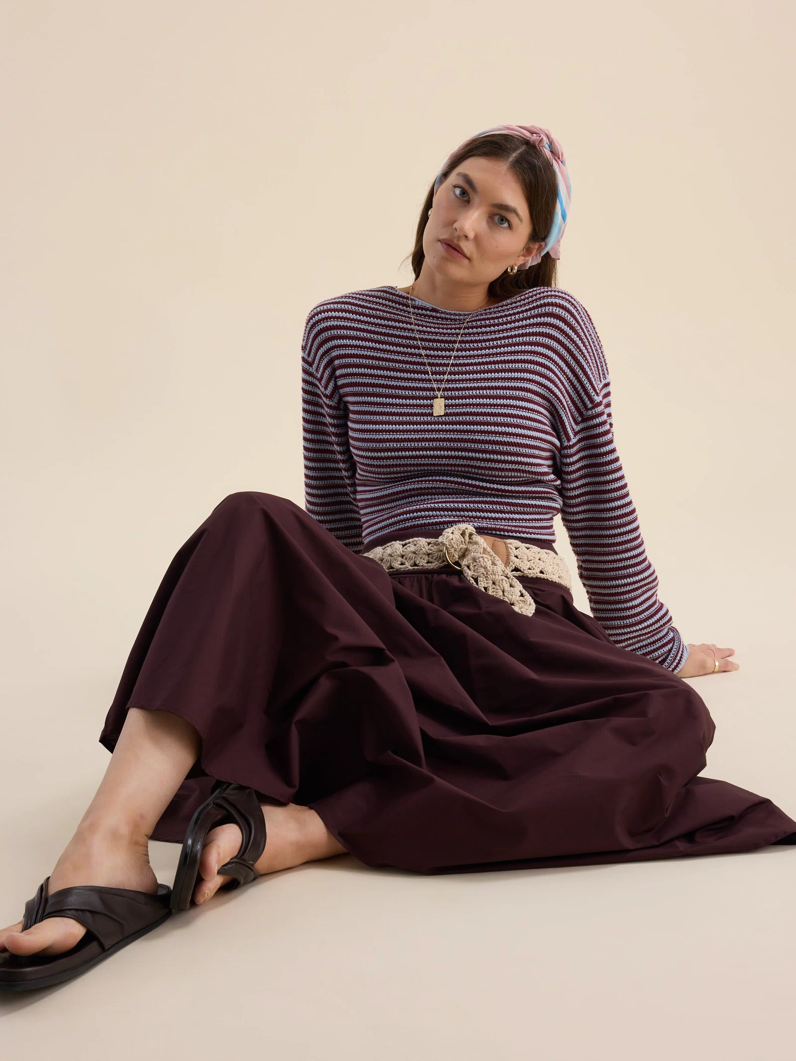 Woman in striped sweater, The Ultimate Skirt by Max, sandals, and headband sits on the floor.