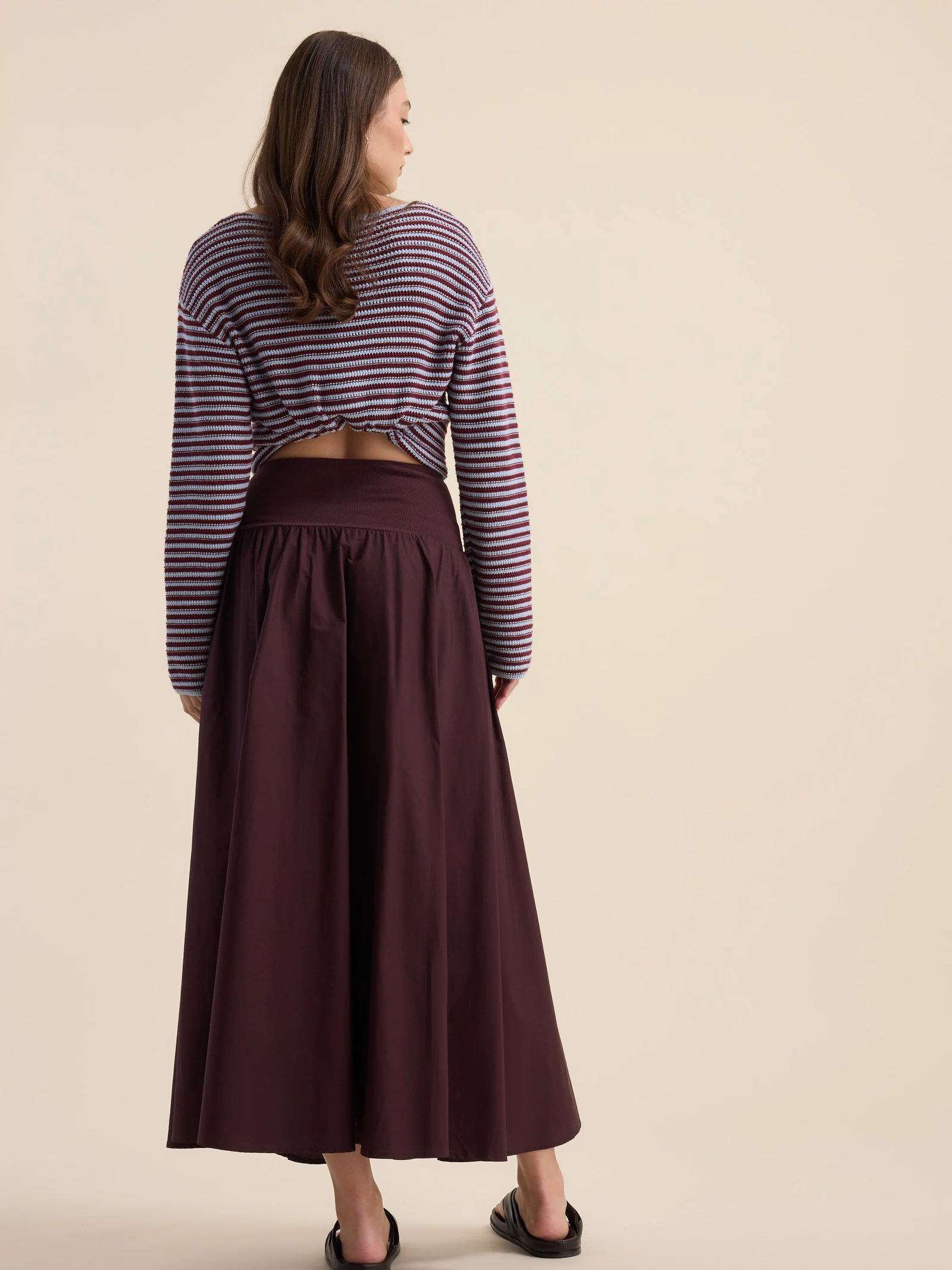 Woman in Max’s The Ultimate Skirt and striped sweater, barefoot by a beige backdrop.