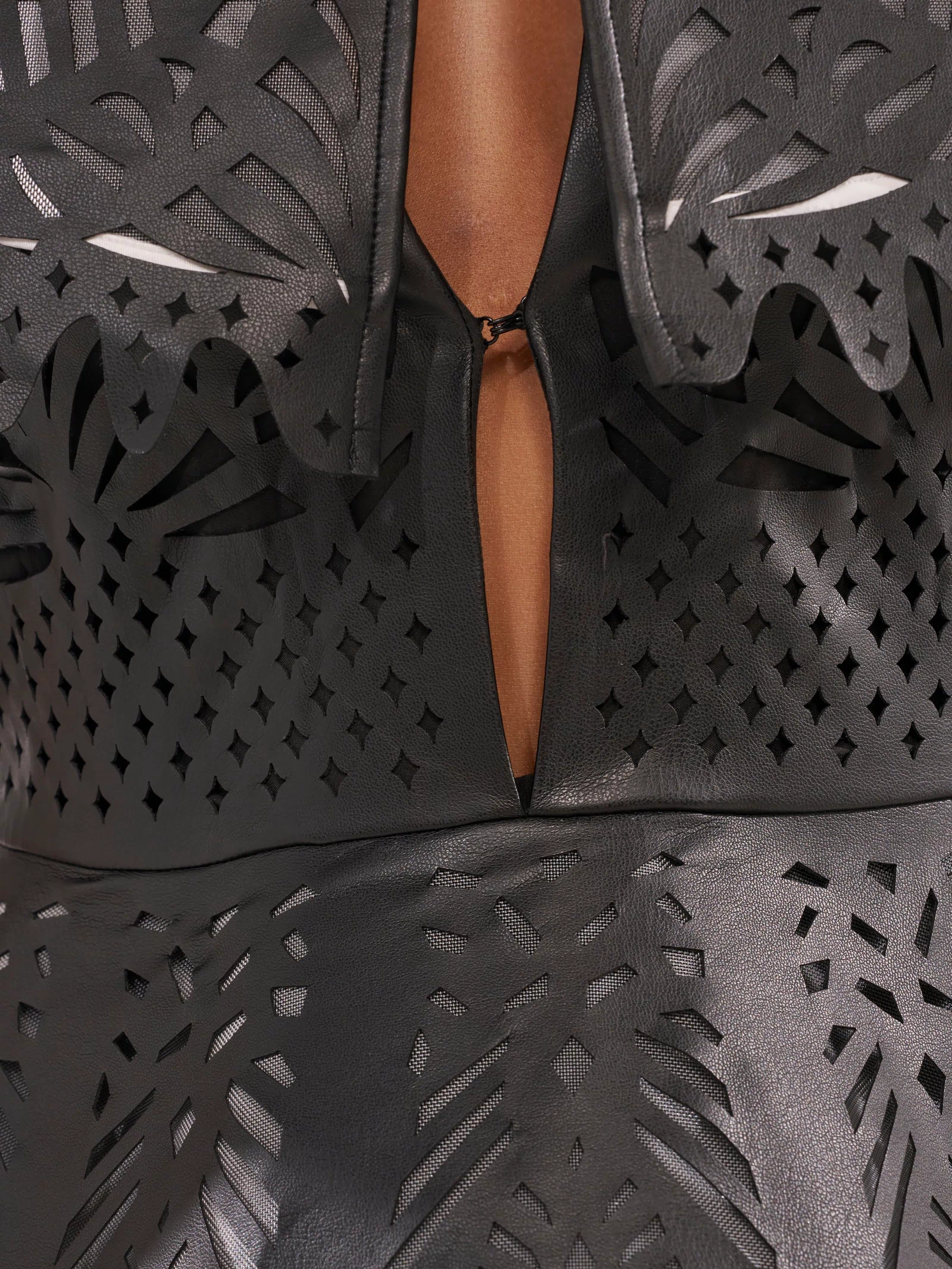 Close-up of the URBAN EDGE MINI COLLARED DRESS in black faux leather, featuring intricate laser-cut patterns and a front keyhole opening. Its glossy finish and bold design make it an ideal statement piece for cocktail parties.