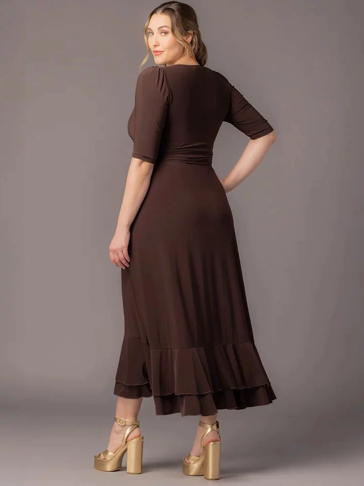 Veronica Ruffled Evening Gown in Chocolate  Back view of a curvy plus size woman against a gray background wearing this Kiyonna maxi dress with 3/4 sleeves, defined banded waist, and a layered ruffle hem. Styled with gold platform sandals.
