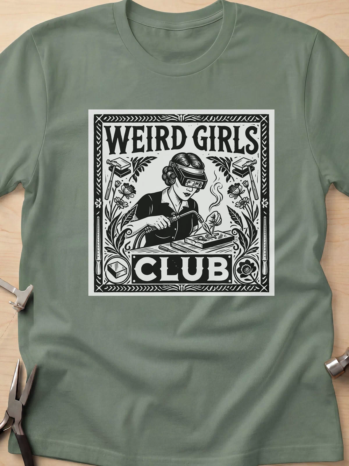 Weird Girls Club funny metalsmith t-shirt in Military Green, flat lay with jeweler's tools