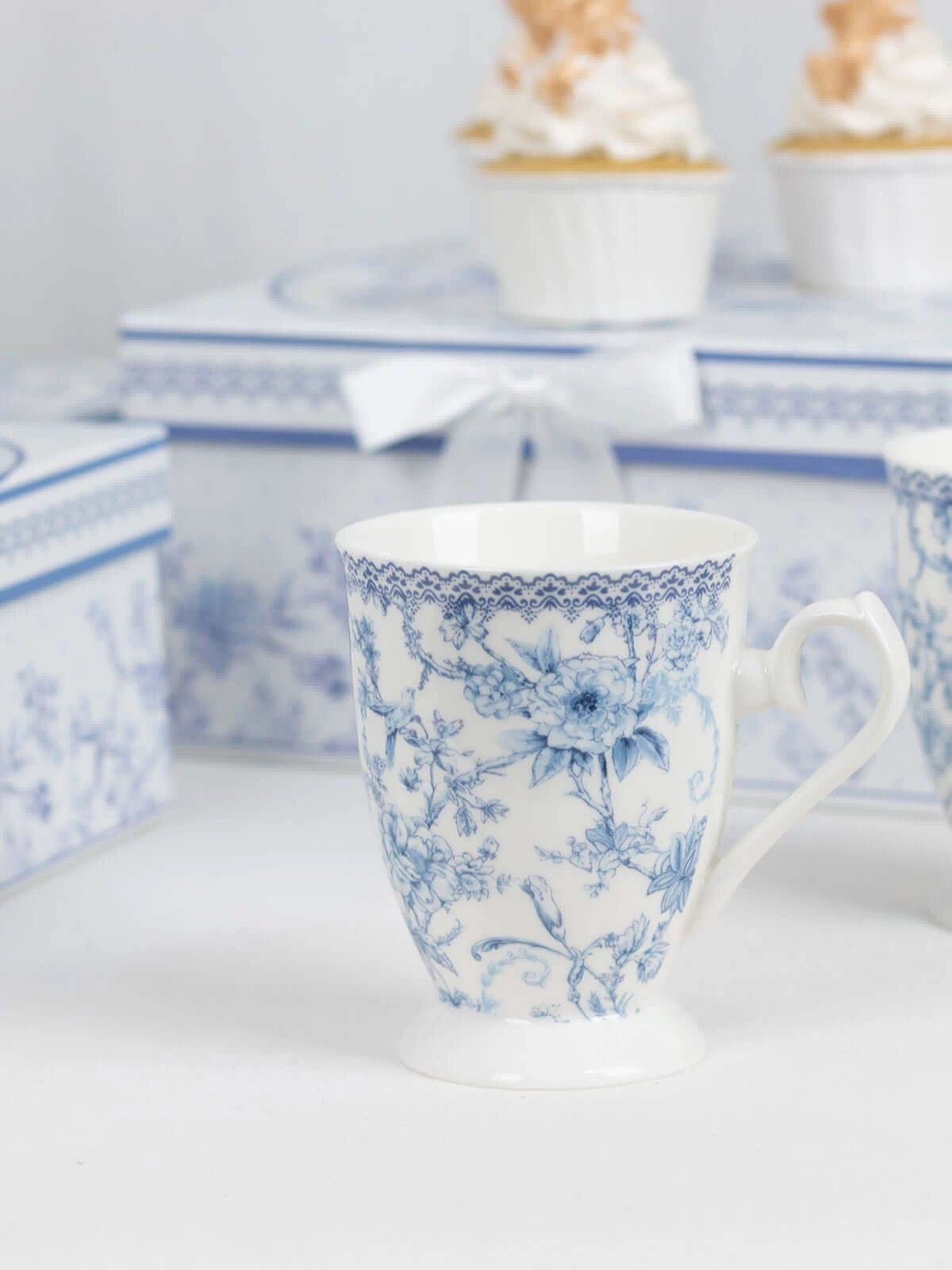 Blue floral porcelain mug with decorative cupcake boxes in the background.