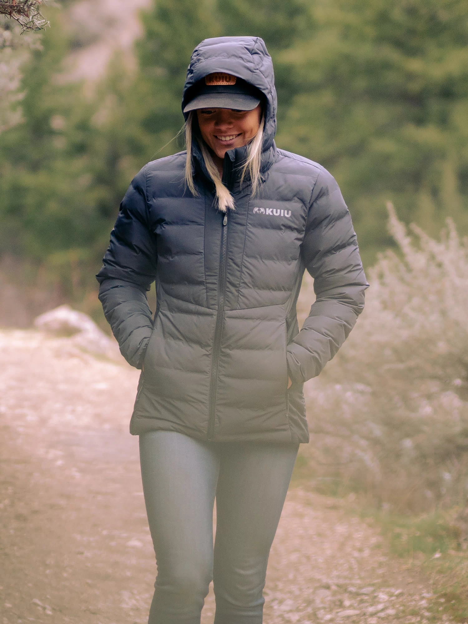Woman wearing Elements Hooded Jacket in Gunmetal with hood on and hands inside zippered hand pockets