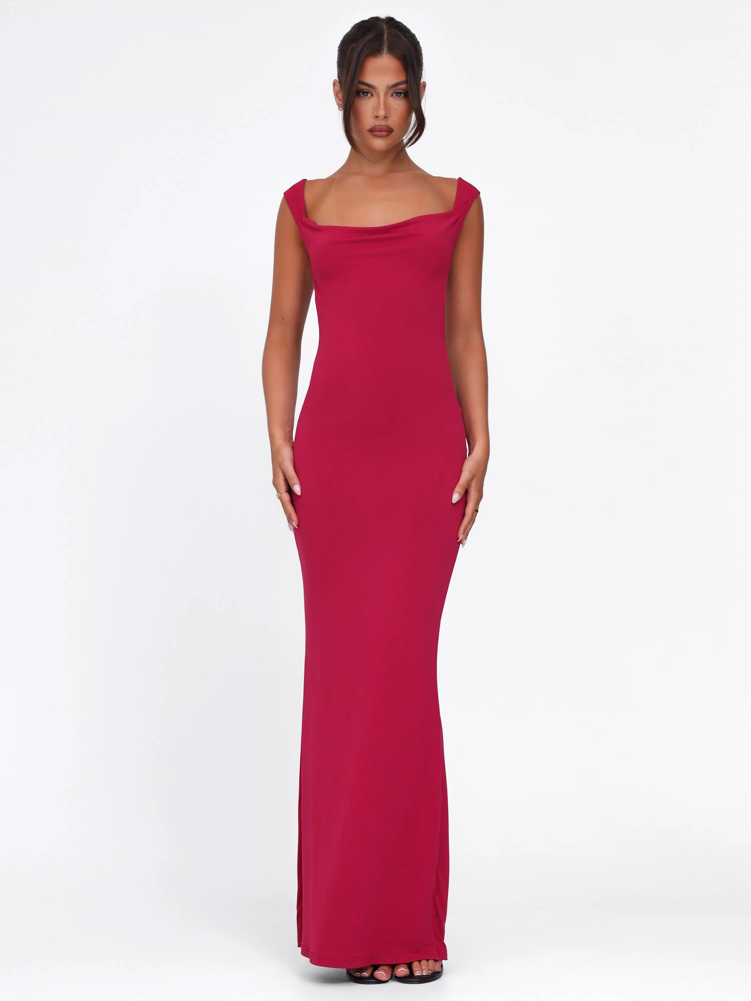 A woman stands against a white background wearing the TIGERMIST ZITA Dress - Red : Salsa : Deep Red, a sleeveless bodycon maxi dress with a slight cowl neckline, styled with black open-toe heels and her dark hair in a center-parted updo.